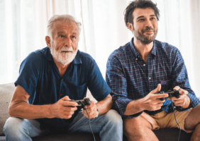 Elderly father and middle aged son play playstation together this Father's Day