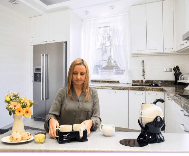 Woman in the kitchen using the Muggi Cup Holder carrying 2 cups of tea