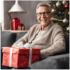 Elderly man sitting in-front of the Christmas tree with a large present on his lap